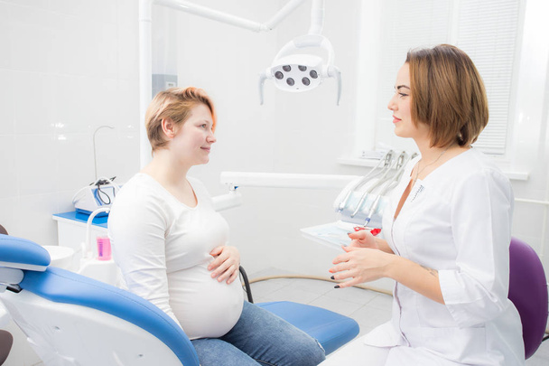 pozitív terhes nő a fogorvosi rendelőben, konzultáció fiatal női fogorvossal. fogászati kezelés terhes nők számára - Fotó, kép