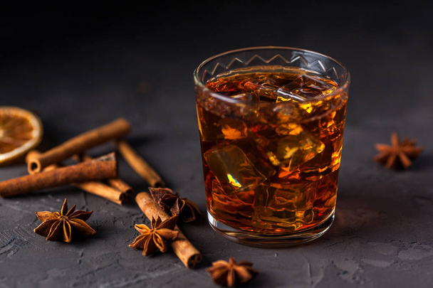 Glass of brandy or whiskey, spices and decorations on dark backg - Фото, изображение