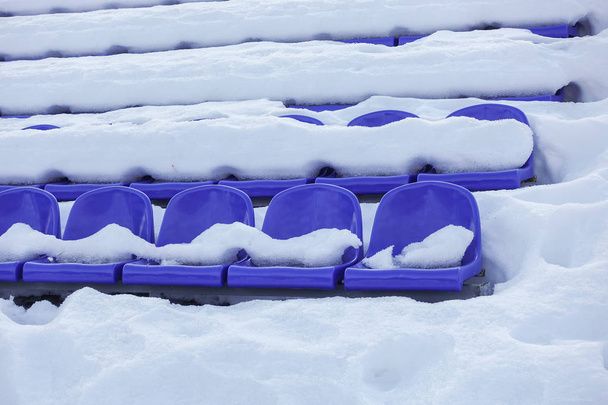 Tribünen im Sportstadion im Winter, Stühle der Fans - leere Tribünen, die vom Schnee bedeckt sind - Foto, Bild