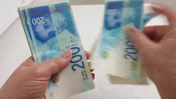 Senior vrouw tellen shekel bankbiljetten van 200 en zet ze op witte tafel - Video