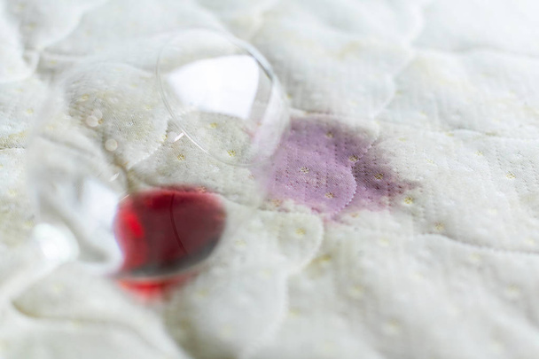 Copa de vino derramada en la cama. Bodegas caídas sobre sábana blanca
. - Foto, Imagen