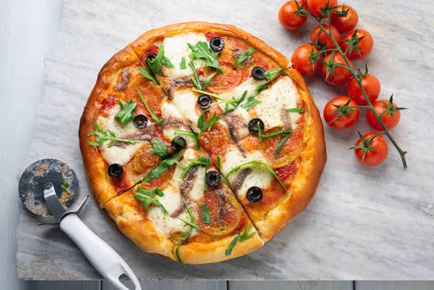 Mozzarella, domates sosu, zeytin, hamsi ve roka salatası ile lezzetli dilimlenmiş sıcak pizza  - Fotoğraf, Görsel