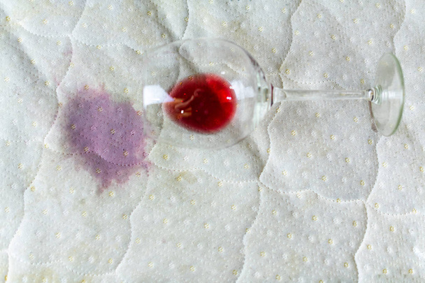 Weinglas auf Bett verschüttet. abgeworfenes Weinglas auf weißem Bettlaken. - Foto, Bild
