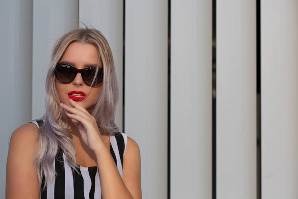 stylisches blondes Mädchen mit roten Lippen und Sonnenbrille posiert in der Nähe - Foto, Bild
