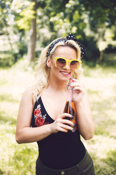 Young woman in sunglasses with drink in park - Foto, imagen