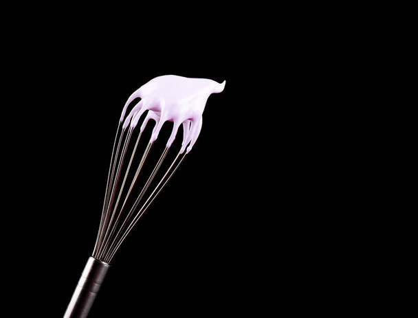 Metal whisk with pink cream isolated on black background. Clipping path. - Photo, Image