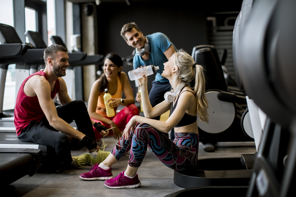 Группа молодых людей в спортивной одежде разговаривают и смеются вместе, сидя на полу спортзала после тренировки
 - Фото, изображение