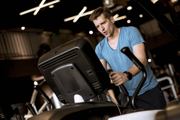 Young man doing exercise on elliptical cross trainer in sport fitness gym club - Photo, image