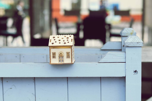 Μικρό παιχνίδι σπίτι στο ξύλινο κιγκλίδωμα του καλοκαιριού καφέ, θολή φόντο - Φωτογραφία, εικόνα