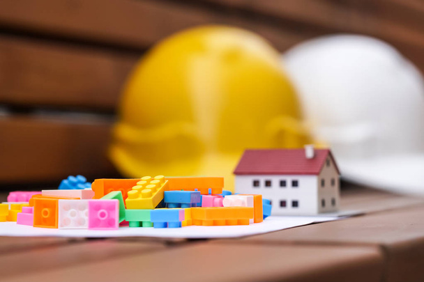 Real estate and new house construction concept. Protective hardhats, house scale model and multicoloured plastic construction toy building blocks or toy bricks. Selective focus - Photo, Image