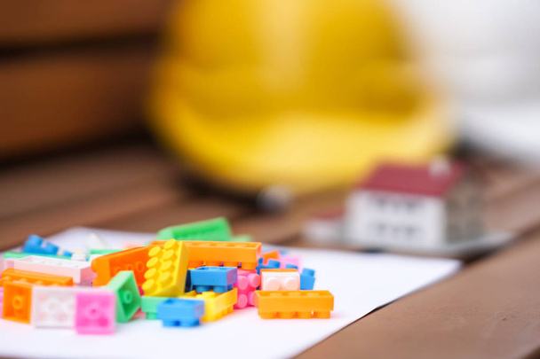 Недвижимость и концепция строительства нового жилья. Защитные каски, модель дома и разноцветные пластиковые строительные строительные блоки или игрушечные кирпичи. Селективный фокус
 - Фото, изображение