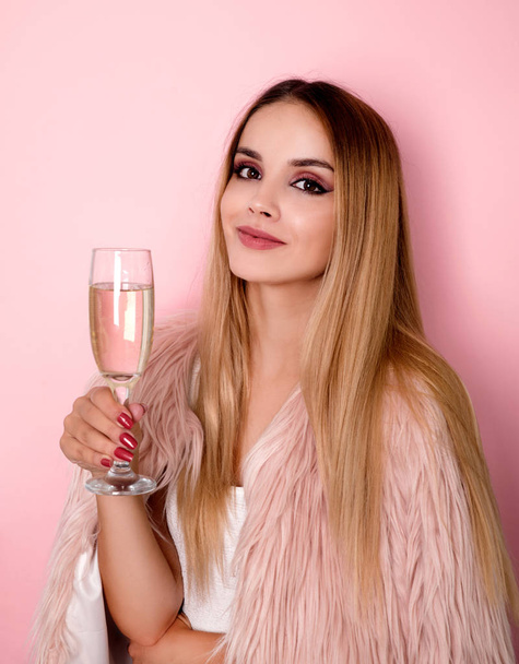 Young woman in pink fur coat holding glass of champagne - Фото, зображення