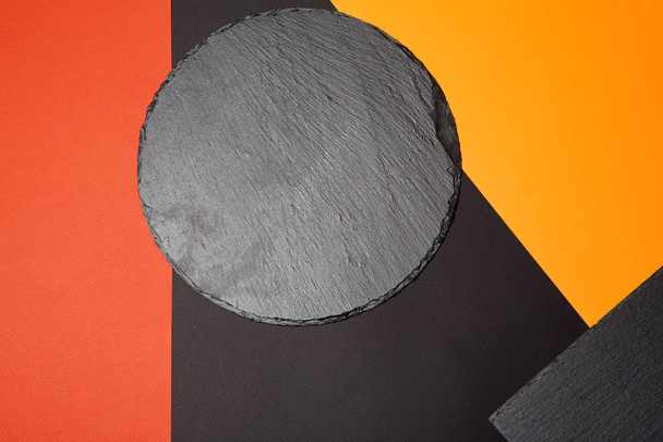 From above of empty black slate serving board on multicolored background with geometric composition - Φωτογραφία, εικόνα