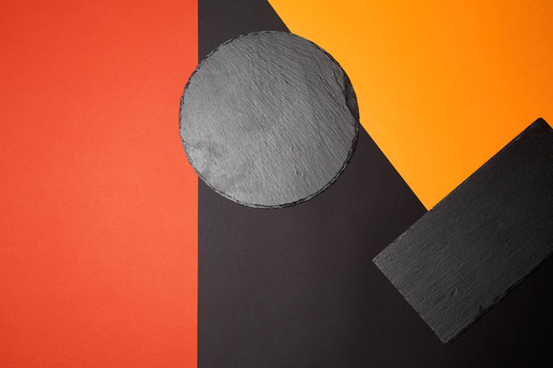 From above of empty black slate serving board on multicolored background with geometric composition - Valokuva, kuva