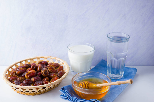 Dried dates, milk and honey on white background. Holy month of Ramadan, concept. Righteous Muslim lifestyle. Starvation. Dates in wooden basket and honey. Vegetarian food. Copy space - Zdjęcie, obraz