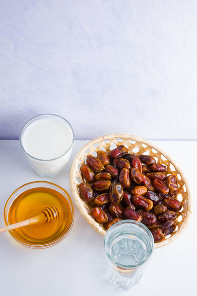 Dried dates, milk and honey on white background. Holy month of Ramadan, concept. Righteous Muslim lifestyle. Starvation. Dates in wooden basket and honey. Vegetarian food. Copy space - Foto, Imagen