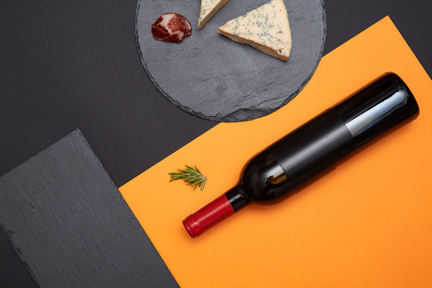 Layout of blue cheese with prosciutto slices on black slate board with bottle of wine on colorful background - Zdjęcie, obraz