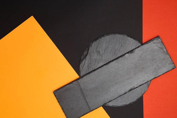 Composition of empty black slate serving board on multicolored background with geometric composition - 写真・画像