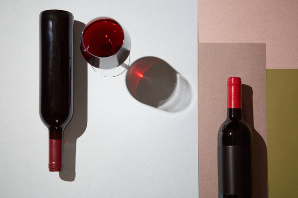 Layout of bottles and glass of red wine on colorful paper background - Photo, Image