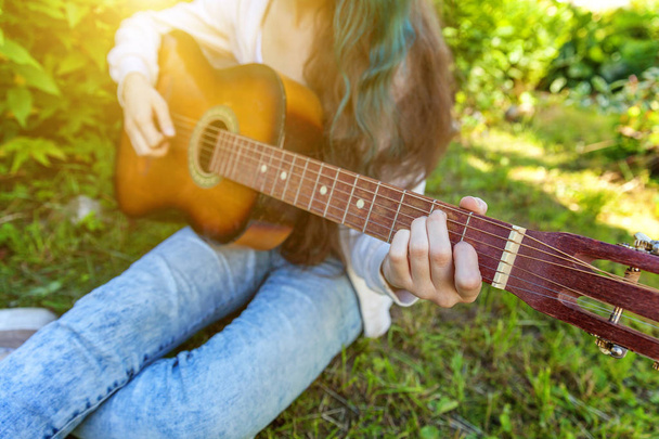 Closeup of woman hands playing acoustic guitar on park or garden background. Teen girl learning to play song and writing music - Foto, afbeelding