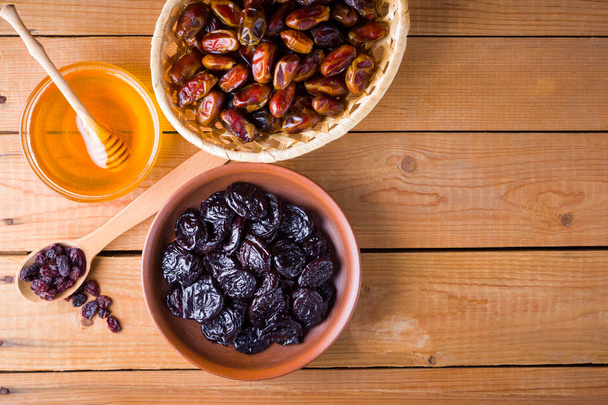 Dried dates, prunes and honey on wooden background. Holy month of Ramadan, concept. Righteous Muslim lifestyle. Starvation. Dried fruits: dates, prunes and raisins on wooden boards - 写真・画像