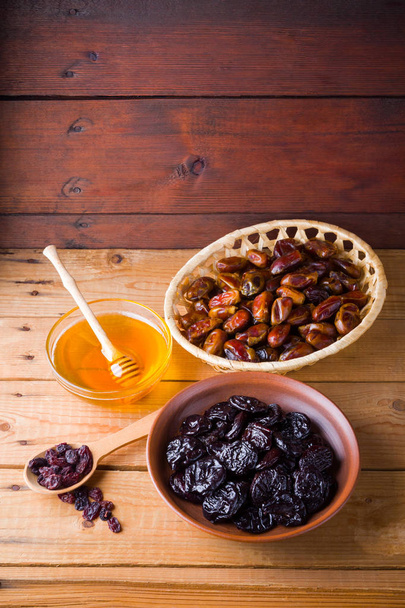 Dried dates, prunes and honey on wooden background. Holy month of Ramadan, concept. Righteous Muslim lifestyle. Starvation. Dried fruits: dates, prunes and raisins on wooden boards - Fotoğraf, Görsel