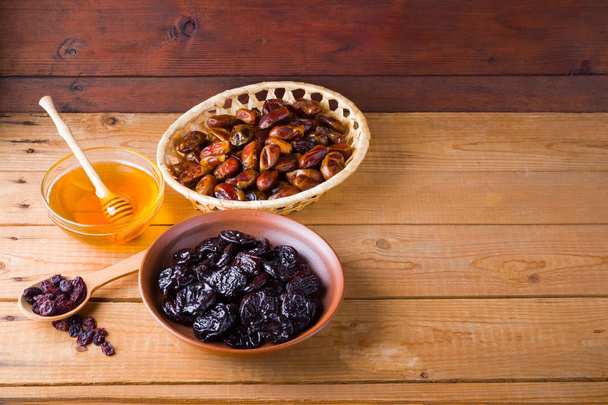 Dried dates, prunes and honey on wooden background. Holy month of Ramadan, concept. Righteous Muslim lifestyle. Starvation. Dried fruits: dates, prunes and raisins on wooden boards - Zdjęcie, obraz