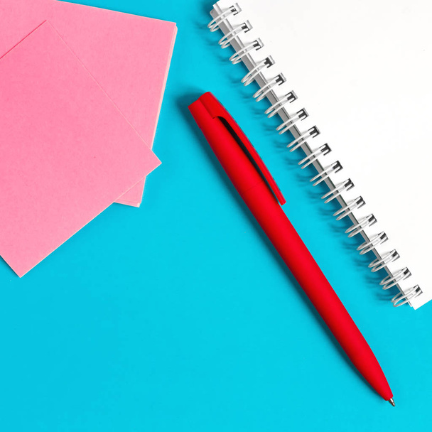 Bloco de notas, papelaria caneta em um fundo azul branco com pétalas de flores vermelhas, conceito de um local de trabalho feminino
 - Foto, Imagem