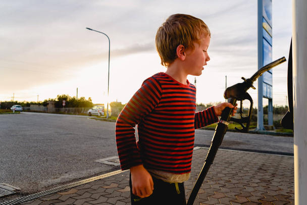 Dítě držící hadici palivového čerpadla při západu slunce u čerpací stanice - Fotografie, Obrázek
