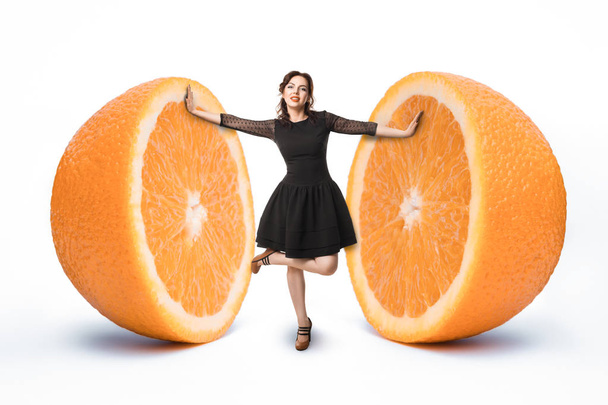 small female between halves of giant orange; woman on diet, - Φωτογραφία, εικόνα