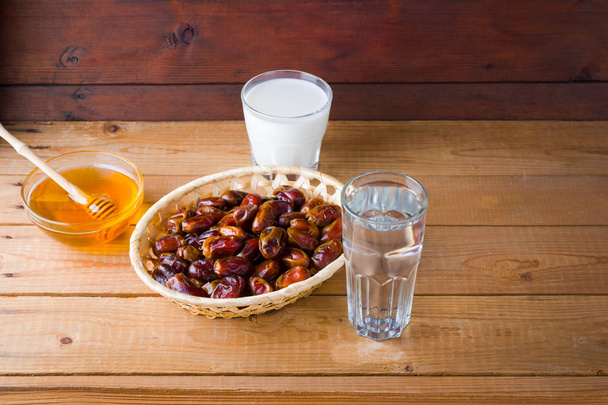 Dried dates, milk and honey on wooden background. Holy month of Ramadan, concept. Righteous Muslim lifestyle. Starvation. Dates in a wooden basket and raisins in the style of minimalism - Fotografie, Obrázek