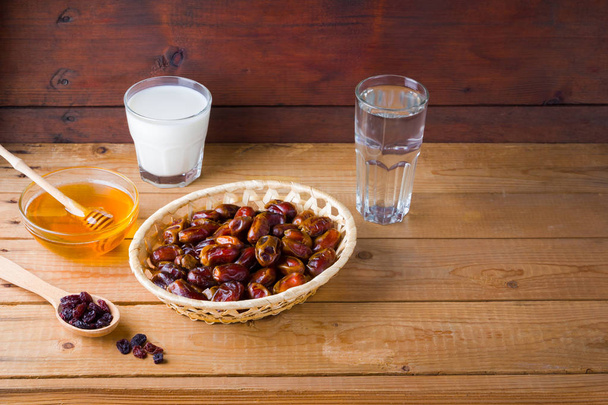 Dried dates, milk and honey on wooden background. Holy month of Ramadan, concept. Righteous Muslim lifestyle. Starvation. Dates in a wooden basket and raisins in the style of minimalism - Foto, Imagem