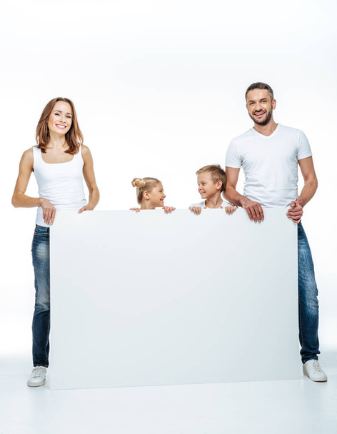 Happy family in white t-shirts holding blank card isolated on white - Fotó, kép