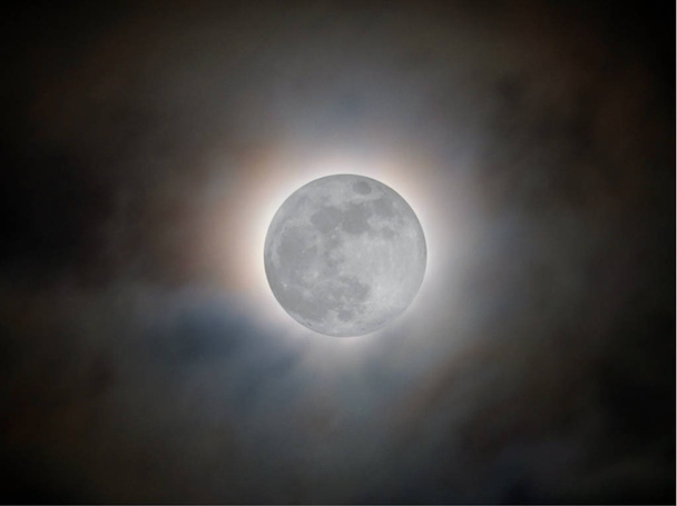 яркая полная луна, окруженная светящимся ореолом и освещенными облаками на черном ночном небе
 - Фото, изображение