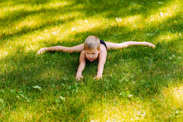 seven-year-old tanned boy in bathing trunks performs acrobatic exercise "cross twine" in the summer outdoors - Zdjęcie, obraz