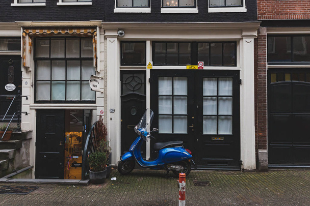 Niebieska skuter zaparkowany przez drzwi budynku w centrum Amsterdamu - Zdjęcie, obraz