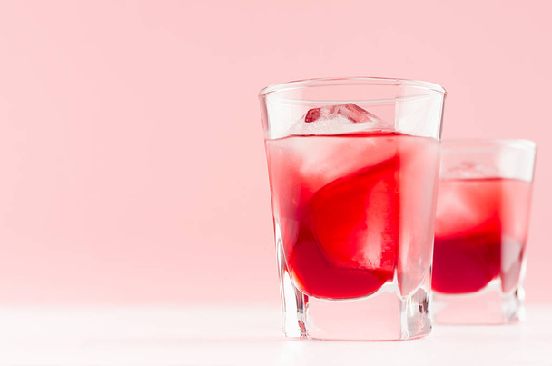 Fresh cold red summer fruit cocktails with ice cubes in elegant modern kitchen interior in light soft pastel pink color on white wood board. - Foto, imagen