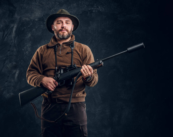 Volwassen hunter met geweer en verrekijkers. Studio foto tegen donkere muur achtergrond - Foto, afbeelding