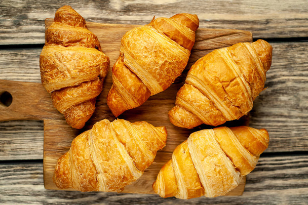 Fresh french croissants on wooden chopping board over old wooden background  - Photo, Image