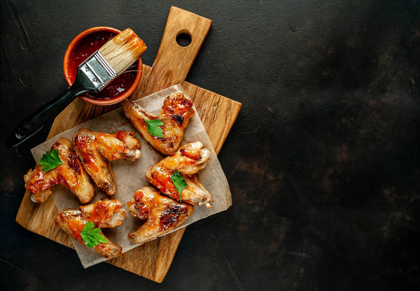 Grilled chicken wings in barbecue sauce with parsley on cutting board over black stone background - Photo, Image