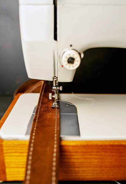 Близкий вид швейной машинки с коричневым кожаным ремнем
  - Фото, изображение