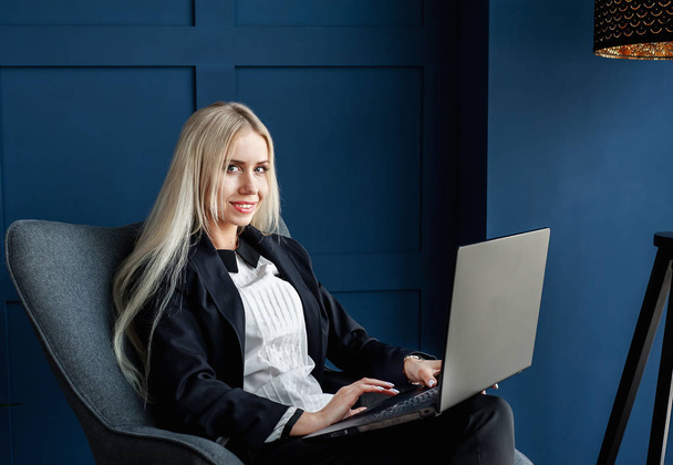 Zarif iş kadını koltukta oturan ve mavi iç dizüstü bilgisayar üzerinde çalışıyor  - Fotoğraf, Görsel