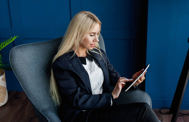 Elegante donna d'affari seduta in poltrona e al lavoro su tablet computer in interni blu
  - Foto, immagini