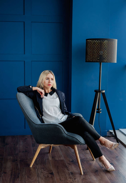 Elegante zakenvrouw zittend in fauteuil in blauwe studio  - Foto, afbeelding