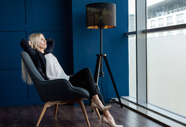 Mavi stüdyoda koltukta oturan zarif iş kadını  - Fotoğraf, Görsel