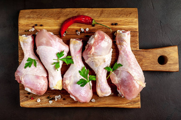 Chicken legs with spices, chili pepper and parsley leaves on wooden chopping board  - Photo, Image
