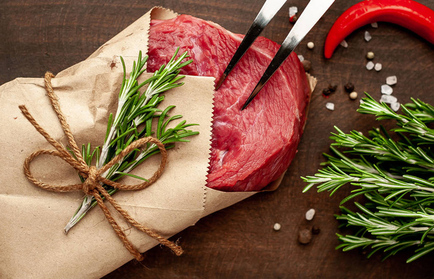 Raw beef steak wrapped in craft paper with rosemary twigs on wooden chopping board - Photo, Image