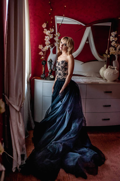 Young blonde woman in elegant evening dress posing in red luxury interior - Photo, Image