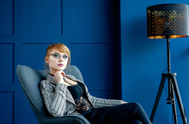 Elegant businesswoman sitting in armchair in blue studio  - Zdjęcie, obraz