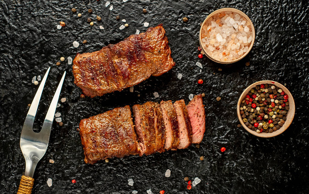 Close view of sliced grilled steaks with spices on stone black background - Photo, Image